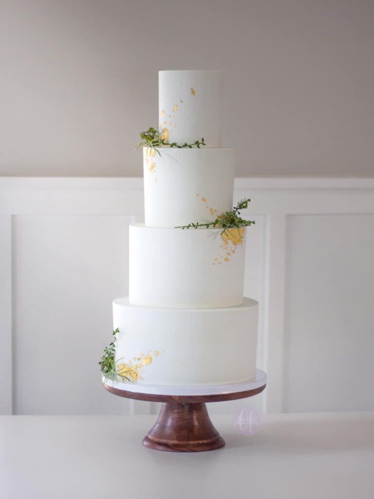 Four-Tier Buttercream Wedding Cake: A clean, simple, and crisp design in sizes 10"-8"-6"-4". Elegantly adorned with gold leaf details and pops of greenery, this wedding cake exudes timeless sophistication and simplicity