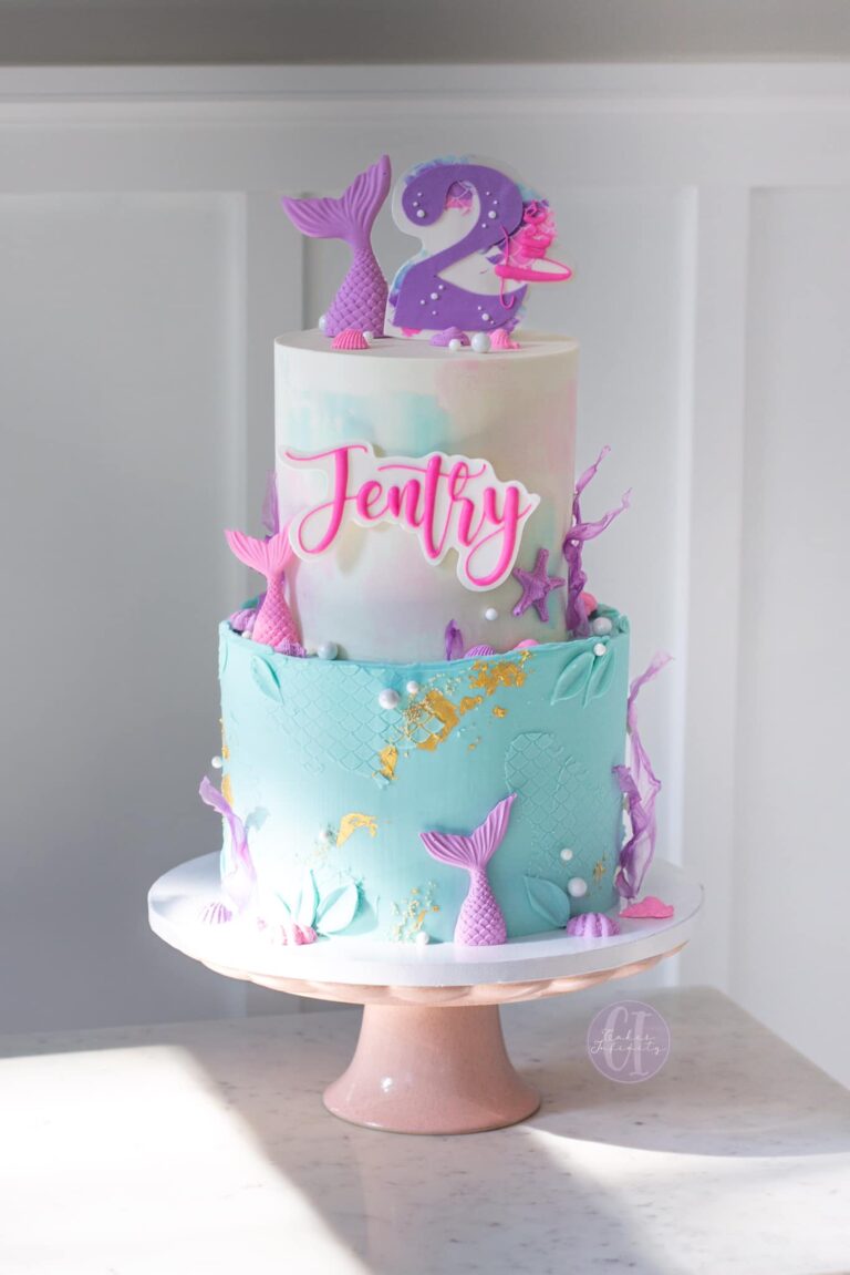 Jentry's 2nd Mermaid Themed Cake: A whimsical delight featuring a 2-tier buttercream cake (8"-6") adorned with enchanting white chocolate mermaid tails. The design captures the magic of an underwater world, making it a perfect centerpiece for a mermaid-themed celebration