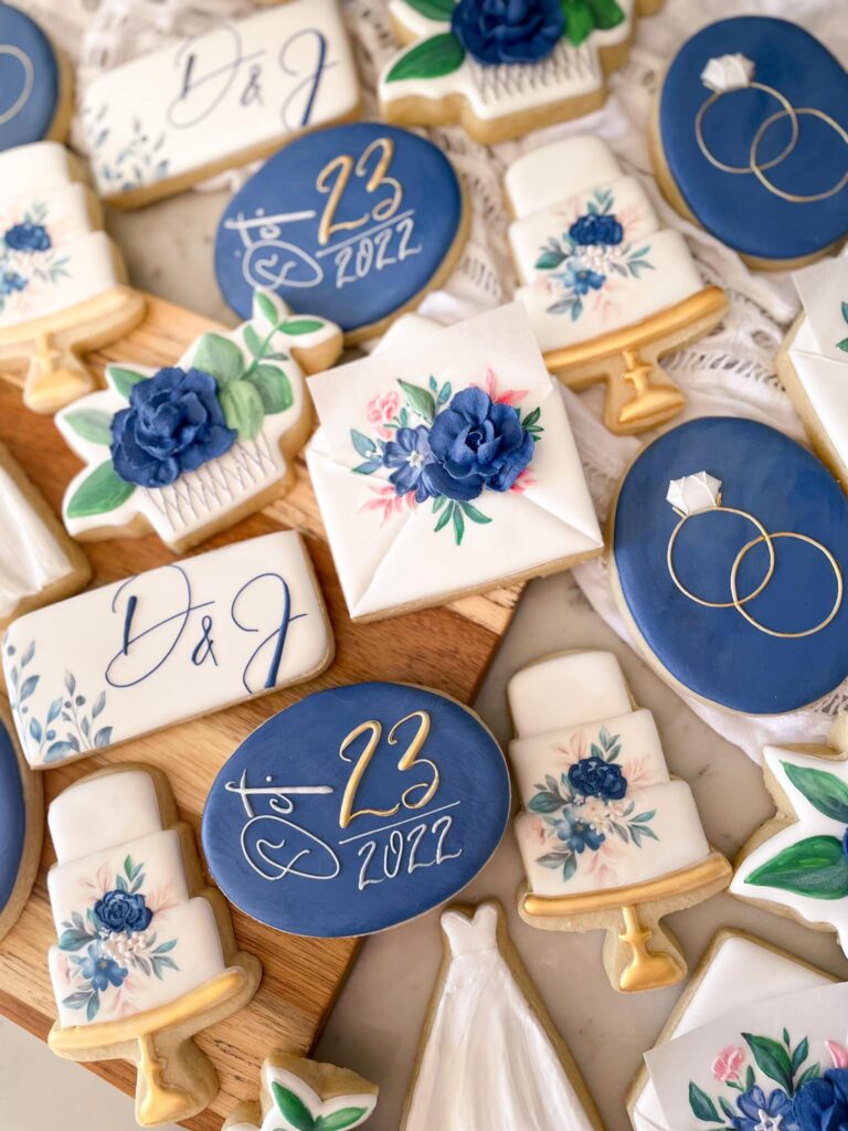 Custom Navy Wedding Cookies: Exquisite handcrafted treats with intricate details, featuring royal icing floral designs, the couple's initials, wedding date, a delicately piped wedding ring, and a miniature wedding cake. These personalized cookies are a delightful and meaningful addition to any wedding celebration