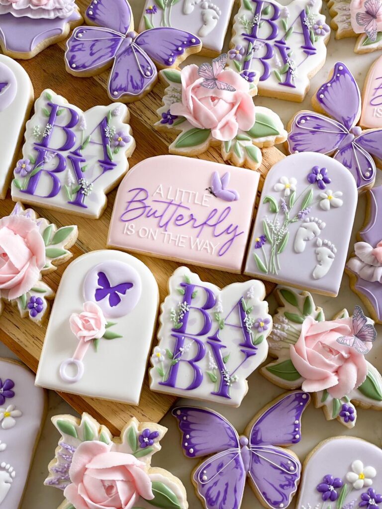 Butterfly Baby Shower Cookies: Exquisite and detailed cookie collection for a baby shower, featuring intricate designs. The cookies showcase wafer paper butterflies, hand-piped royal icing floral patterns, and artfully crafted fonts. The color scheme, incorporating lavender, purples, and white, adds a touch of elegance to this beautiful and tasteful treat display