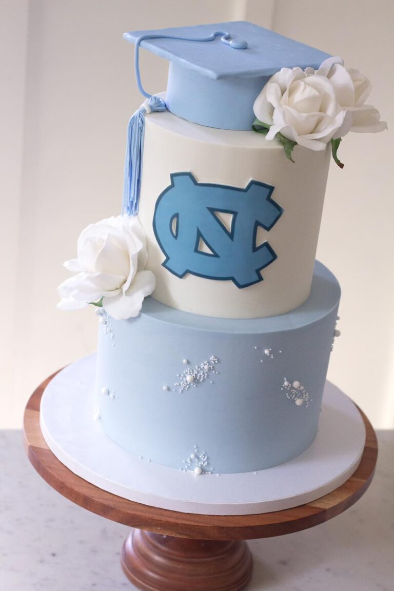 UNC Graduation Cake: An elegant 8"-6" cake with a small cap cake on top, celebrating a UNC graduation. The design features classic Chapel Hill blue colors, white roses, and pearl detailing, creating a modern, clean, and floral vibe for this special academic achievement celebration