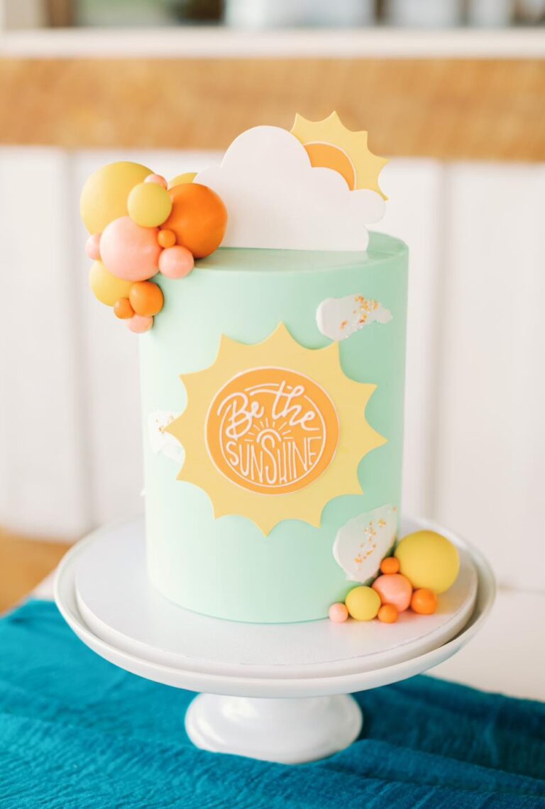 Sunshine Themed Cake: A tall and slim 6" double barrel cake, feeding up to 24 portions. The light blue cake features cheerful sun detailing, playful clouds, and faux balloon decorations, creating a fun and happy vibe for this delightful sunshine-themed celebration