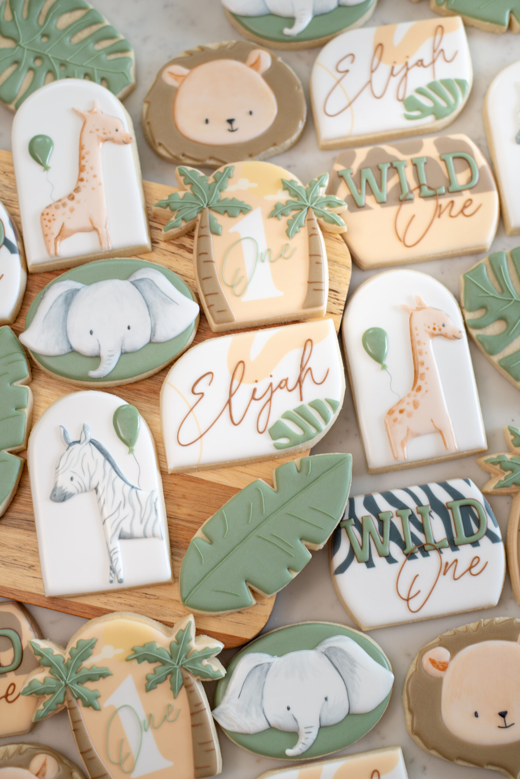 Elijah's Wild One Cookies: Adorable and uniquely designed treats featuring details of leaves and safari animals, including a zebra, giraffe, and lion. These super cute cookies are perfectly coordinated to match the cake, creating a charming dessert table assortment for Elijah's Wild One celebration